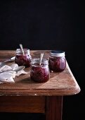 Raspberry jam in three screw top glass jars on a wooden table