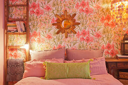 Ladder leant against floral wallpaper and used as bedside table in bedroom