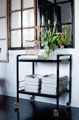 Magazines on serving trolley on black floor below interior window