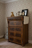 Battered, antique chest of drawers against vintage-style beige wallpaper