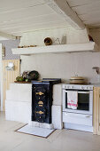 Cooker and old wood-fired stove below extractor hood in country-house kitchen