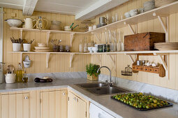 Shelves mounted on wall panelling painted yellow in country-house kitchen