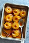 Roasted pears in a pan with caramel sauce, vanilla pod and cinnamon stick