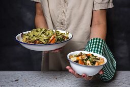 A woman holding two bowls of green tagliatelle with seafood