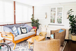 Day bed and coffee table made from recycled wood, and two rattan armchairs in the living room with white wood paneling