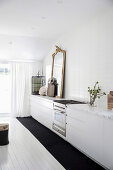 weiße Küchenzeile mit antikem Goldrahmenspiegel und Käfig, weißer Holzdielenboden