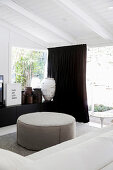 White sofa and ottoman, sideboard with antique vessels and dark curtain in front of the patio door