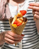 An ice cream cone filled with chocolate and fruit salad for a summer picnic