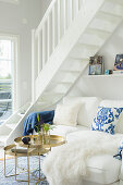 White couch with scatter cushions and set of round tray tables below staircase