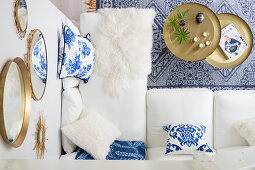 Blick von oben auf weiße Couch mit Kissen und Lammfell und runden Tabletttisch-Set