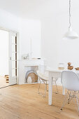 White dining area: dining table and classic chairs on wooden floorboards with disused fireplace in corner