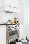 Gas cooker with extractor hood in white kitchen with black and white chequered marble floor tiles