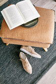 Aufgeschlagenes Buch auf braunem Fußhocker und beigefarbene Schuhe