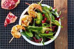 A prawn skewer on avocado salad with pomegranate seeds