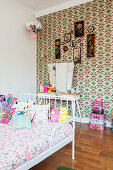 Scatter cushions and soft toys on white bed in girl's bedroom with retro wallpaper