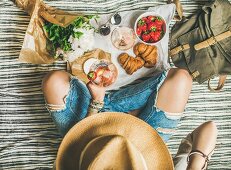 Frau in Jeans mit Weinglas, Erdbeeren und Croissants auf Picknickdecke (Aufsicht)