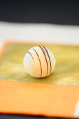 A white truffle praline decorated with fine chocolate stripes