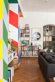 Colourful partition with wide stripes, black leather couch and book shelves