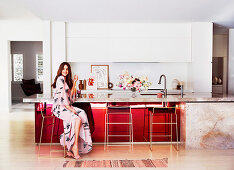 Junge Frau sitzt an eleganter Küchentheke mit Marmorabeitsplatte und roter Front