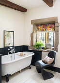 Free-standing bathtub and black classic chair in rustic bathroom