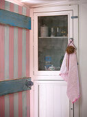 Blick durch rosa-weiss gestrichener Holztür auf Vitrinenschrank mit Küchenutensilien