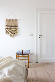 Hand-made wall hanging on white wall in bedroom with wooden floorboards