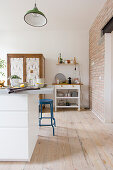 weiße Kücheninsel und blauer Barhocker in offener Küche mit Holzdielenboden und Ziegelwand