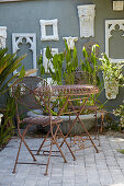 weiße Bilderrahmen an grauer Wand, Grünpflanzen, Tisch und Stühle im Innenhof
