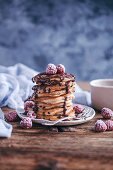 Stack of banana pancakes topped with chocolate drizzle and frozen raspberries