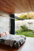 Double bed in the bedroom with concrete wall, wooden ceiling and terrace access