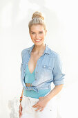 A young blonde woman with a bun wearing a bodysuit, white trousers and a denim shirt