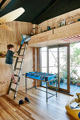 Loft bed made of wood, boy on the ladder, including football table in front of balcony door