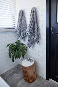 Handtücher, Zimmerpflanze und Baumstamm-Hocker im Badezimmer mit weißen Wandfliesen