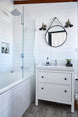 Vanity unit next to bathtub with shower screen in white tiled bathroom