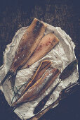 Herring fillets with chives and pink pepper on parchment paper with a knife and fork