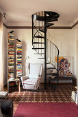 Vertical bookshelves and armchair next to spiral staircase in reading area