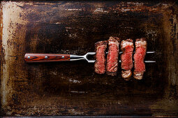 Slices of grilled meat barbecue steak, Rib eye on meat fork on dark metal background