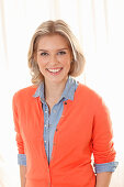 Junge blonde Frau in Jeanshemd und orangefarbener Strickjacke