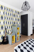 Modular shelves and guitar against geometric wallpaper and fitted wardrobe in teenager's bedroom