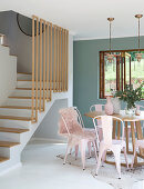 Round dining table and pink metal chairs at foot of staircase