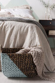 Diagonally painted basket with a knitted plaid in front of the bed