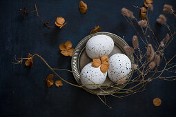 Dried flowers around speckled eggs on pewter plate