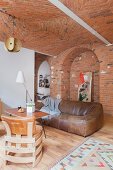 Designer leather chairs, coffee table and leather sofa in open-plan interior with brick ceiling, brick wall and partition wall