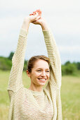 A young woman stretching in a meadow wearing a a knitted jumper