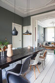 Long dining table and classic chairs in dining room with dark wall and white wooden floor