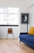 Blue sofa, standard lamp and chair below window in living room with herringbone parquet floor