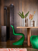 Designer-Stehleuchte, Holztisch mit Vasen und Kerzenhaltern und grüner Panton-Stuhl vor Wand mit dunkler Holzverkleidung