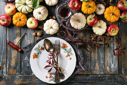 Autumn holiday table decoration setting with decorative pumpkins, apples, red leaves, empty plate with vintage cutlery