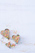 A set of three heart cookie cutters filled with colorful sprinkled on a white surface