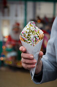 A hand holding a bubble waffle with candy canes and pistachios (Christmas)